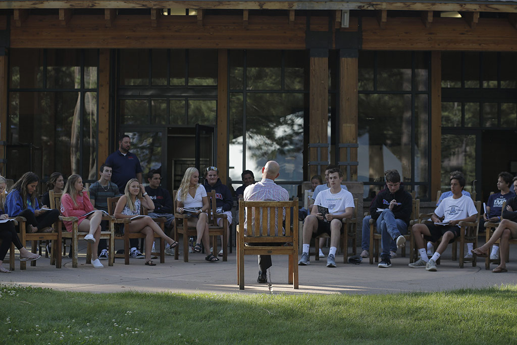 a group of students at a Launch event sitting in chairs outside with an instructor in front of them all speaking to them